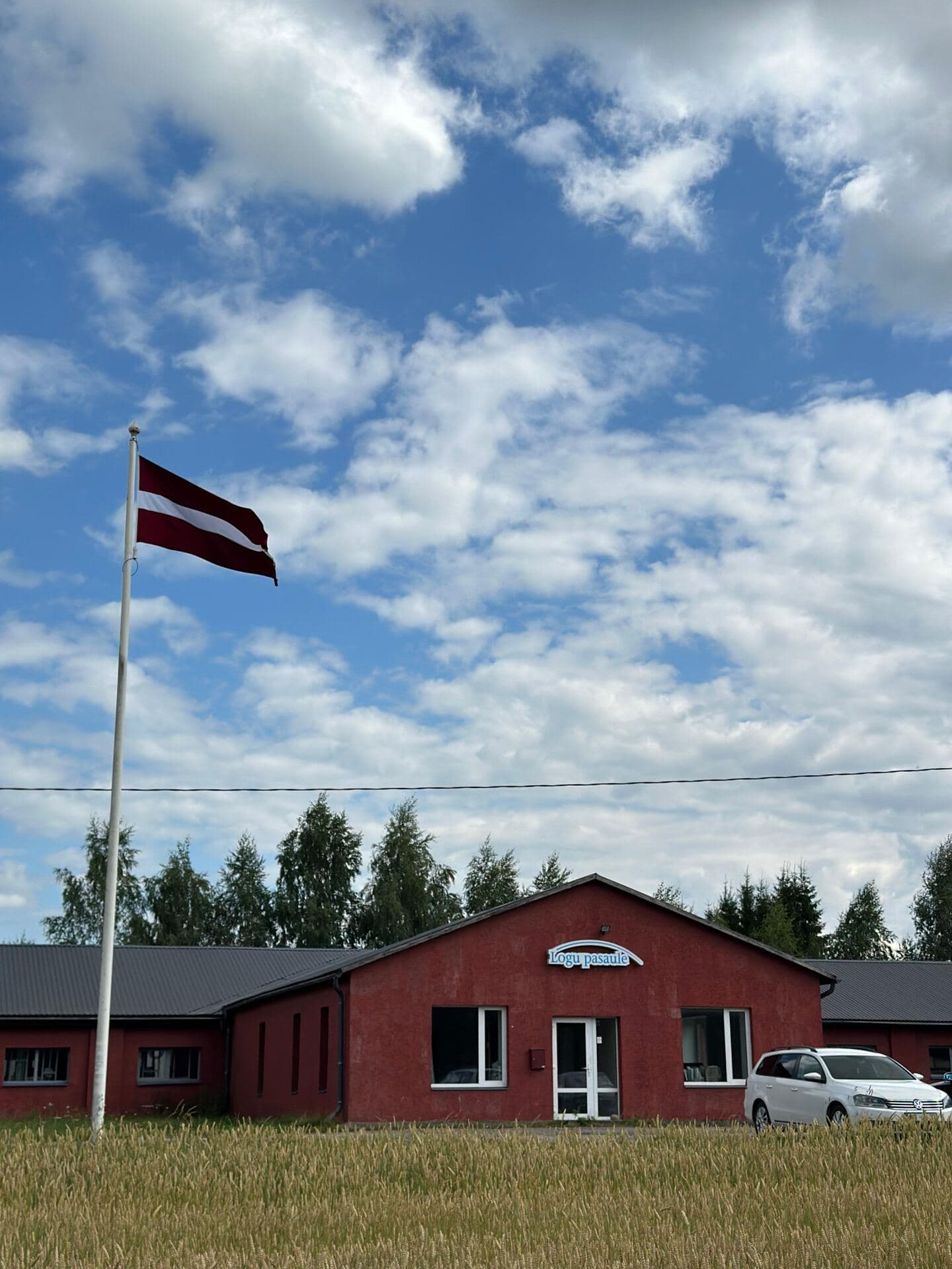 Logu Pasaule ražotne Stalbē, Cēsu novadā — sarkana ražošanas ēka ar Latvijas karogu